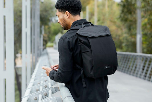 Black backpack on Black man standing on a bridge using a cellphone