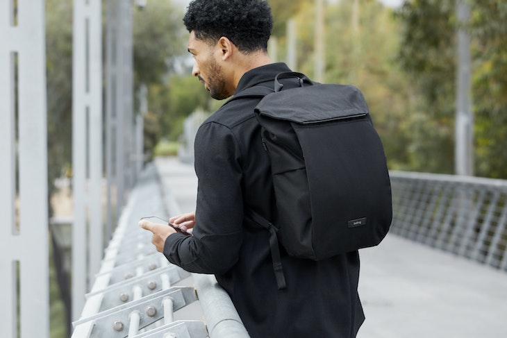 Black backpack on Black man standing on a bridge using a cellphone
