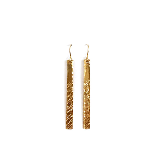 Long gold barred earrings with texture running low to high, left to right, photoed on a white background