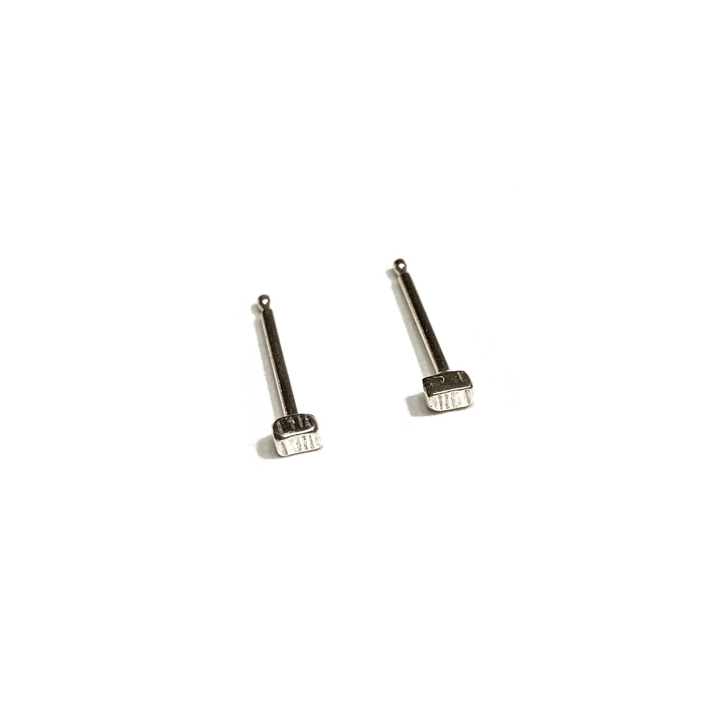 Two tiny silver textured stud earrings and posts angled on a white background