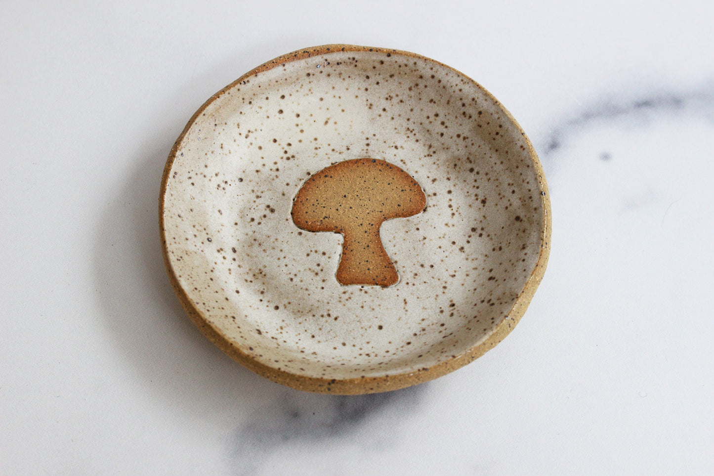Speckled ceramic plate with a mushroom-shaped object on a marble surface
