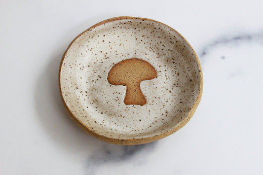 Speckled ceramic plate with a mushroom-shaped object on a marble surface