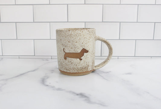 Speckled ceramic mug with dachshund silhouette on a marble surface with white tiled wall background
